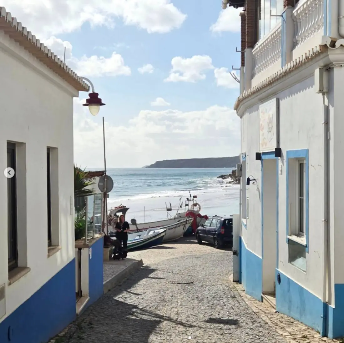 Whitewashed Salema fishing village street leading down to the beach and fishing boats